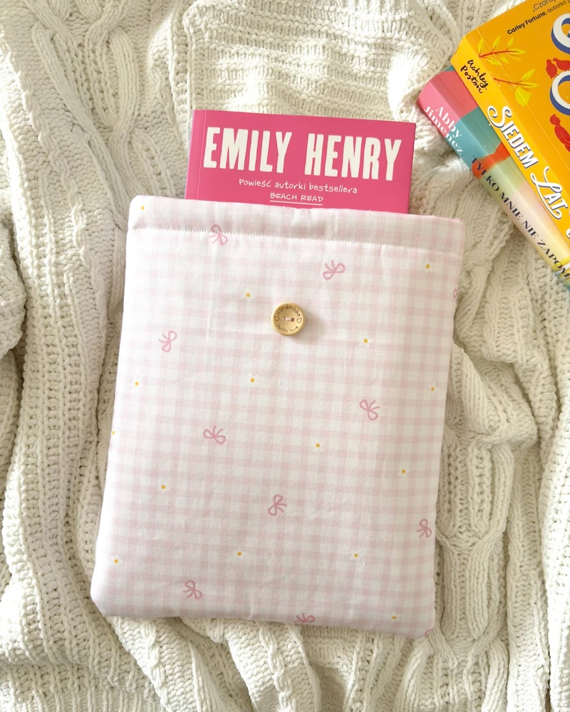 Etui na książkę Romansiara w drobną różową kratkę vichy, z książką Emily Henry, na kocu