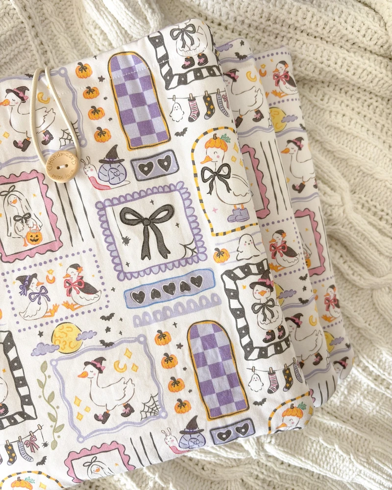 Booksleeve halloweenowe gąski, ze wzorem w gąski, duszki i dynie, ułożone w stos