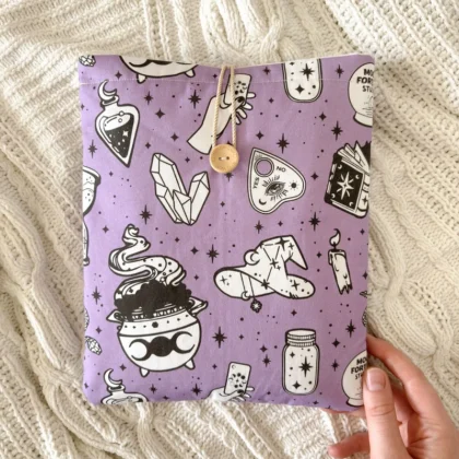 Booksleeve Kocioł czarownic w fiolecie ze wzorem w eliksiry, kociołki i gwiazdki, ułożony na kocu