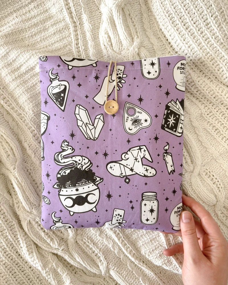 Booksleeve Kocioł czarownic w fiolecie ze wzorem w eliksiry, kociołki i gwiazdki, ułożony na kocu