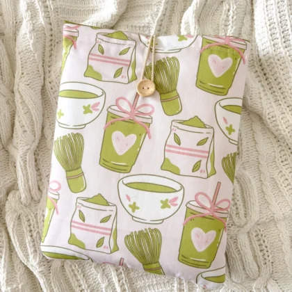Booksleeve z wzorem w zielone kubeczki matcha, ułożone na kocu