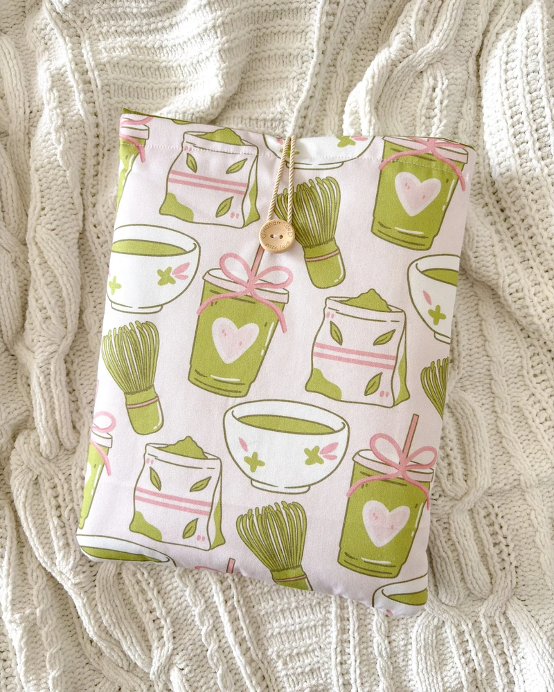 Booksleeve z wzorem w zielone kubeczki matcha, ułożone na kocu