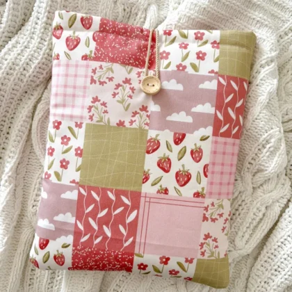 Booksleeve Patchwork w różowym patchworkowym wzorze z truskawkami i kwiatkami, ułożone na kocu