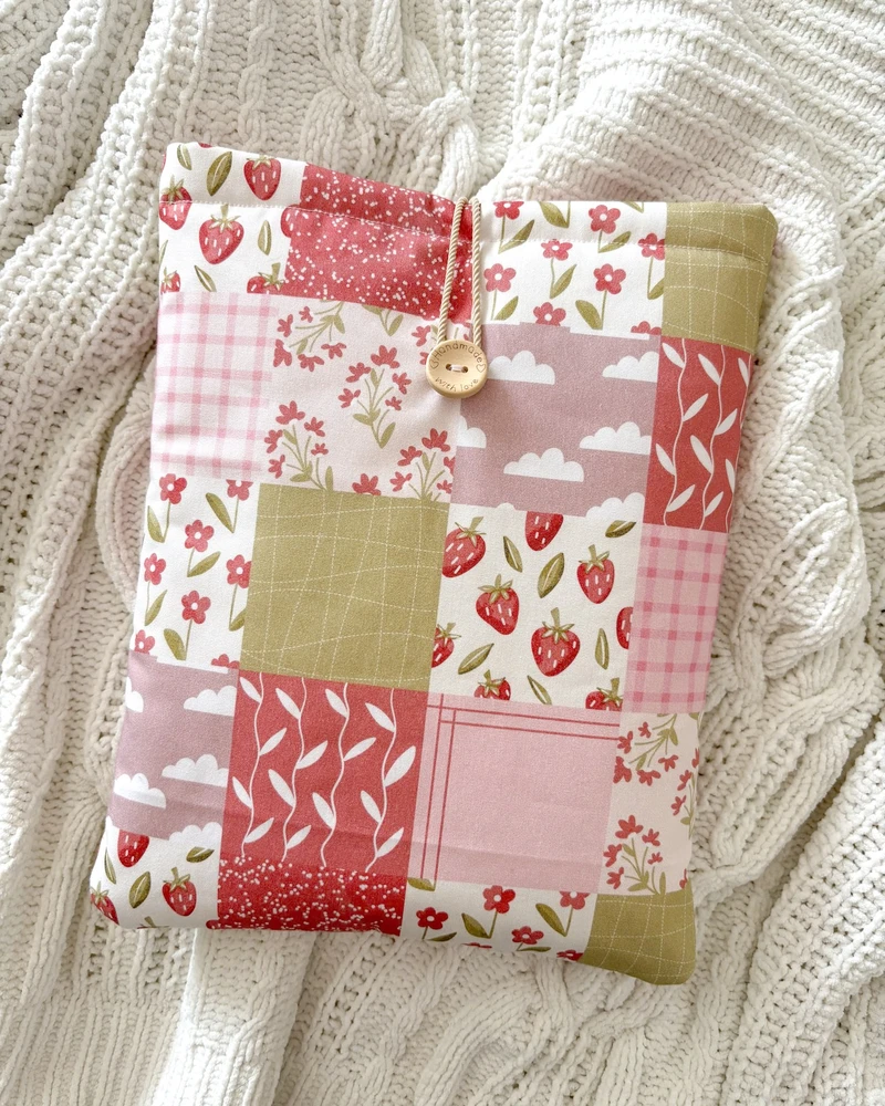 Booksleeve Patchwork w różowym patchworkowym wzorze z truskawkami i kwiatkami, ułożone na kocu