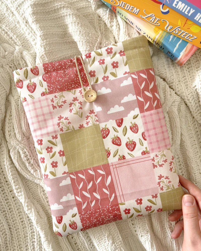 Booksleeve Patchwork w różowym patchworkowym wzorze z truskawkami i kwiatkami, obok stosu książek