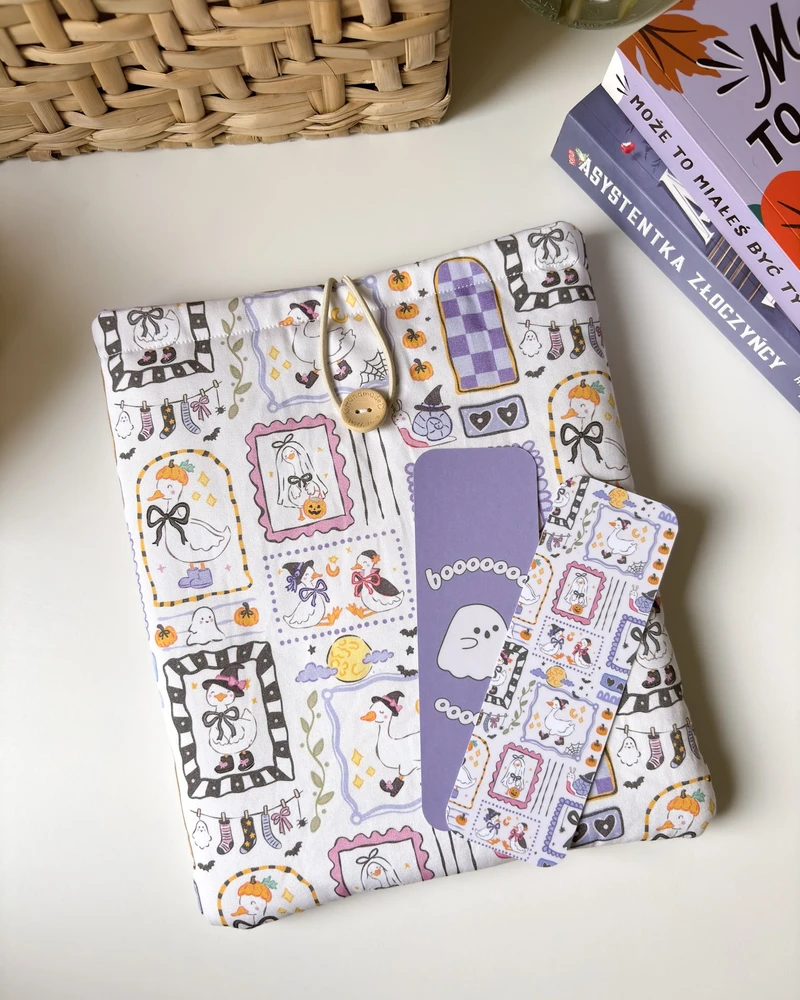 Etui na książkę Halloweenowe gąski w jasnym fiolecie, obok pasujących zakładek, na tle wiklinowego kosza